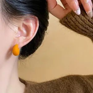 Detailed macro shot of vibrant orange flocked C-shaped stud earrings worn on an ear