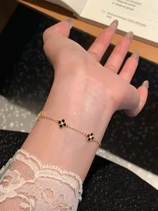 Close-up of elegant gold flower bracelet with black clover charms on wrist.