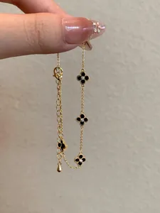 Close-up detail of gold-plated adjustable bracelet with black clover charms and zircons.