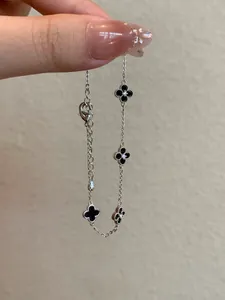 Detailed view of a silver clover bracelet with black enamel motifs held by hand