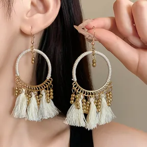 Detailed view of bohemian style gold hoop earrings with white thread tassels and beads