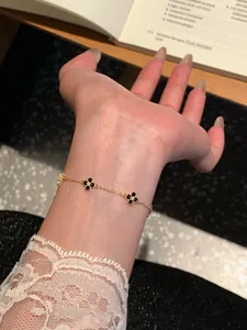 Close-up of gold plated bracelet with black four-leaf clover charms on wrist.