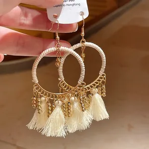 Detailed view of bohemian style circular hoop earrings with cream tassels and gold beads