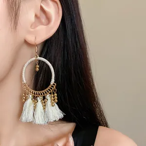 Close-up view of bohemian hoop earrings with white tassels and gold beads on model.
