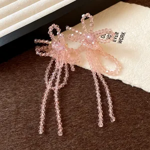 Dettaglio di eleganti orecchini a perno con perle rosa, fiocchi e nappe in perline.