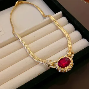 Close-up of vintage gold snake chain necklace with oval red gemstone and rhinestones