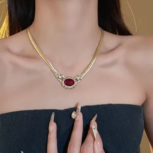 Detail showing a vintage gold snake chain necklace with a red gemstone on a model.