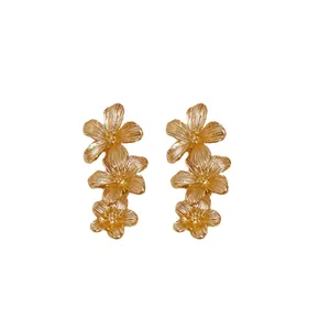 Elegantes pendientes de botón con triple flor dorada y pétalos de metal texturizados.