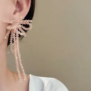 Orecchini a fiocco in perle di vetro rosa pesca con lunghe nappe mostrate sul modello.