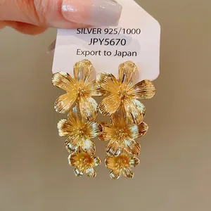 Detalle de pendientes de flores doradas de tres capas con pernos de plata S925 brillante.