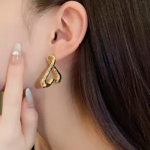 Detalle de un pendiente de corazón retorcido dorado con textura usado en la oreja.