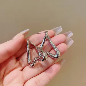 Primer plano de pendientes plateados con forma de corazón irregular y textura metálica