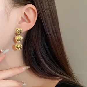Vista detallada de elegantes pendientes de tres corazones de oro con bordes texturizados