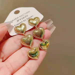 Vista detallada de los pendientes de triple corazón dorado con bordes de cuentas.