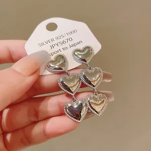 Vista detallada de elegantes pendientes largos de tres corazones en metal plateado