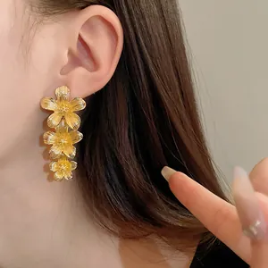 Primer plano de pendientes de flores doradas en la oreja, detalle de textura metálica.