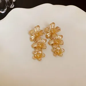 Primer plano de pendientes de flores doradas de tres niveles con texturas detalladas