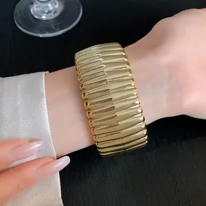 Close-up of gold textured geometric open bangle on wrist with satin sleeve.
