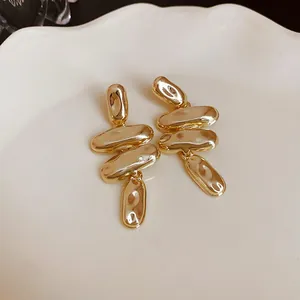 Vista detallada de elegantes pendientes largos dorados de metal irregular sobre un plato cerámico