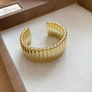 Detail view of a chunky gold-toned ribbed open cuff bracelet in a neutral display tray