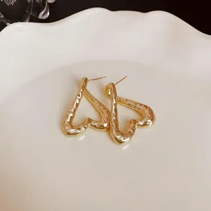 Detalle de pendientes de corazón dorados martillados con acabado en plato blanco