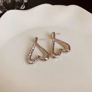 Primer plano de pendientes de corazón plateados con textura martillada sobre plato crema.