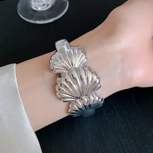 Detailed macro view of a stylish silver shell-textured acrylic cuff bracelet worn on a wrist