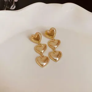 Pendientes colgantes de tres corazones dorados con bordes texturizados y aguja de plata