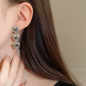 Detalle de primer plano de elegantes pendientes de triple corazón plateados en una modelo