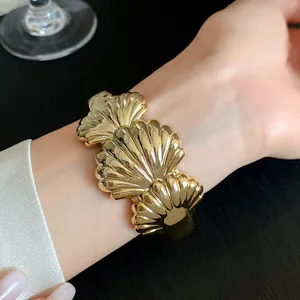 Close-up detail of a golden shell-textured open bangle bracelet worn on the wrist