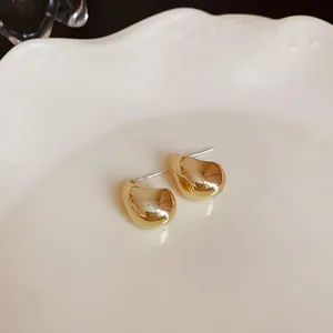 Primer plano detallado de pendientes de botón dorados en forma de haba sobre un plato