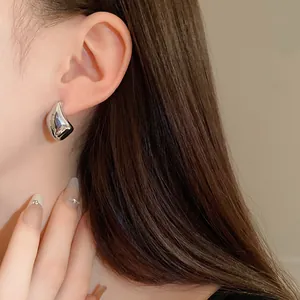 Primer plano de pendientes de tuerca de metal irregulares con acabado plateado brillante.
