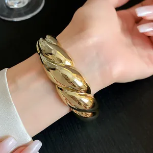 Detail view of a chunky twisted gold acrylic cuff bracelet worn on a woman's wrist