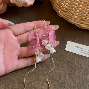 Gros plan d'élégantes boucles d'oreilles en maille avec fleurs de muguet et glands dorés.