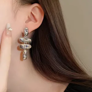 Primer plano detallado de un pendiente colgante de metal plateado irregular en la oreja.