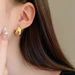 Primer plano de una modelo que luce pendientes de botón de metal dorado con forma gota.