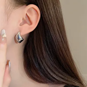 Primer plano de pendientes de gota plateados minimalistas en una oreja de modelo.