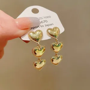 Detalle de pendientes largos de tres corazones dorados con bordes de cuentas.