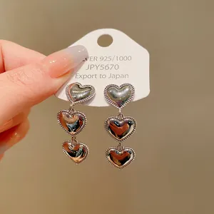 Detalle de elegantes pendientes de triple corazón de plata sobre tarjeta blanca