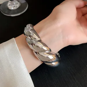 Detail of a chunky silver-colored twisted open bangle bracelet with metallic shine