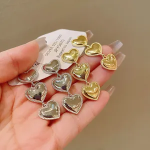 Detalle de pendientes colgantes de triple corazón metálico con agujas de plata 925.