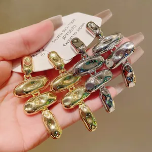 Detalle de los pendientes de frijoles metálicos ondulados en acabados oro y plata
