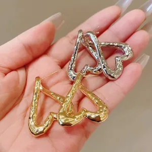 Primer plano de pendientes de corazón con textura de metal martillato en oro y plata