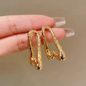 Primer plano de pendientes de metal líquido dorado con diseño de ondas irregulares