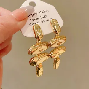 Primer plano de elegantes pendientes colgantes metálicos dorados irregulares con brillo