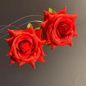 Primo piano dettagliato di orecchini a rosa in tessuto rosso con gocce di rugiada