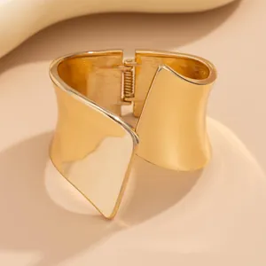 Close-up detail of a minimalist wide asymmetric gold metal cuff bracelet with matte finish.