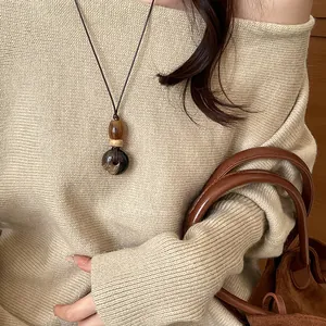 Vintage wood pendant necklace with minimalist design shown on a beige sweater model