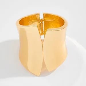 Detailed view of an asymmetric wide gold-plated metal cuff bracelet with hinge closure