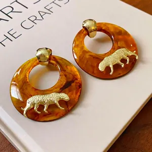 Orecchini a cerchio in resina vintage con motivo tigre dorato, su sfondo di un libro d'arte